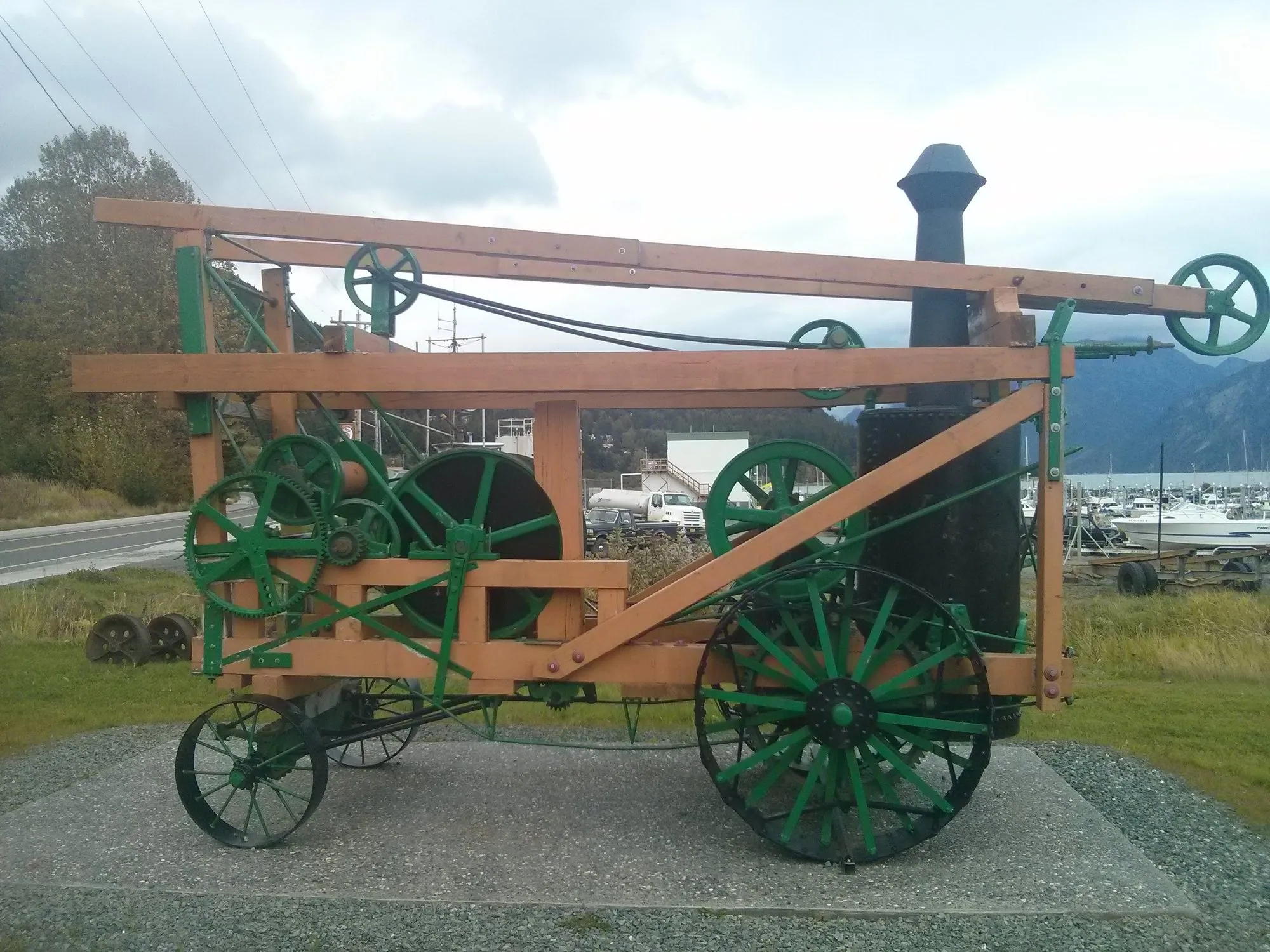 The Keystone Driller on display in Haines, a green-painted steam drilling rig on iron wheels with a timber frame, vertical boiler and stack, the harbour and mountains behind