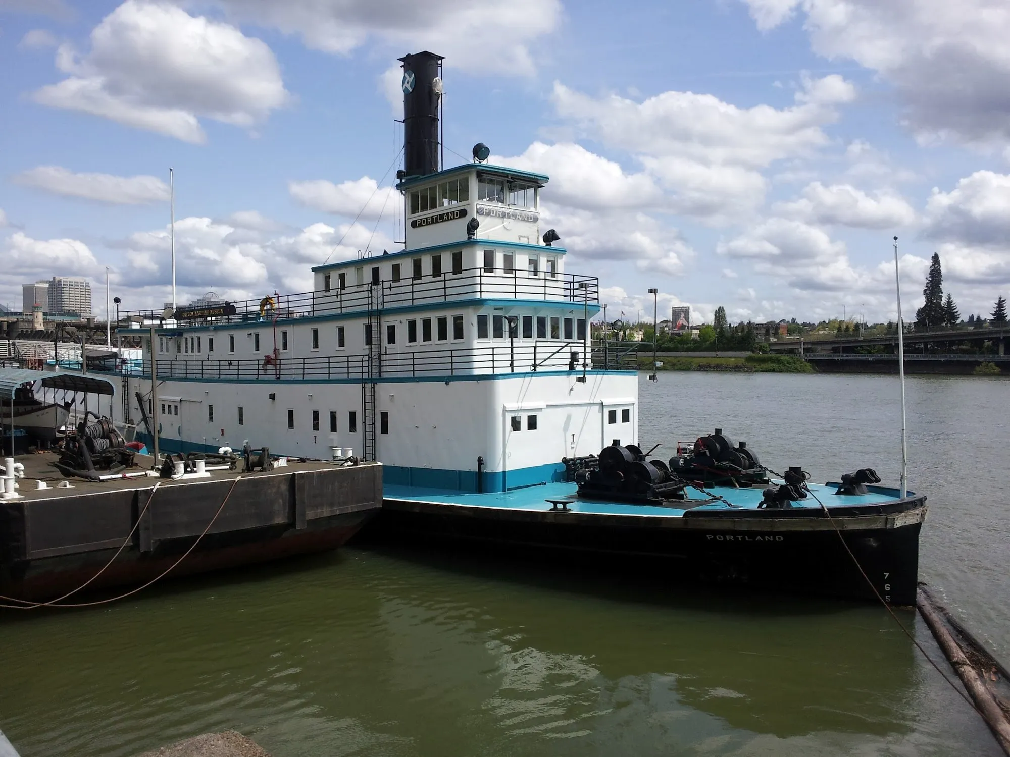 The Portland moored on the Willamette River at Portland, white superstructure with blue trim and a black stack, capstans on her blue foredeck