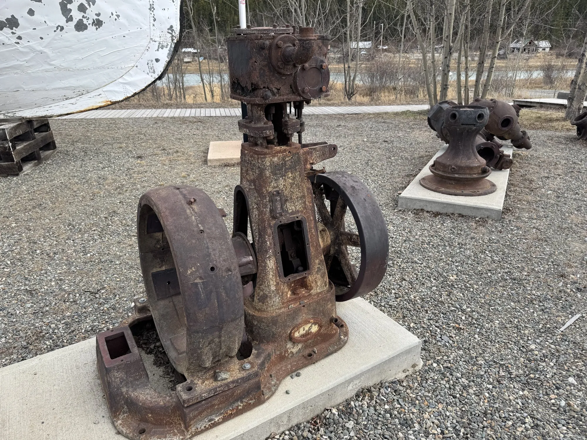 Small rusted vertical machine with two flywheels on a concrete pad
