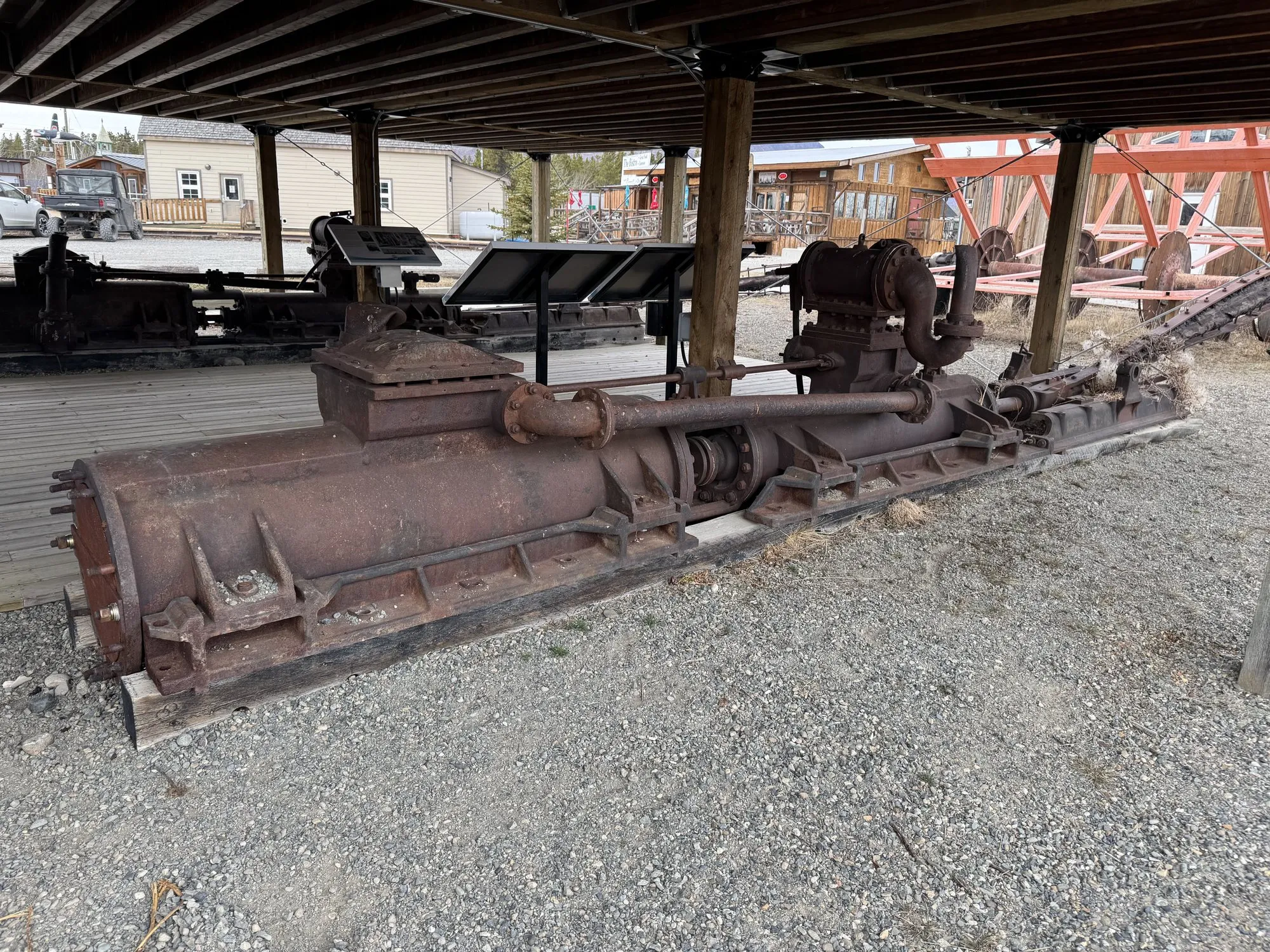 Rusted horizontal steam engine lying on its bed under a timber shelter